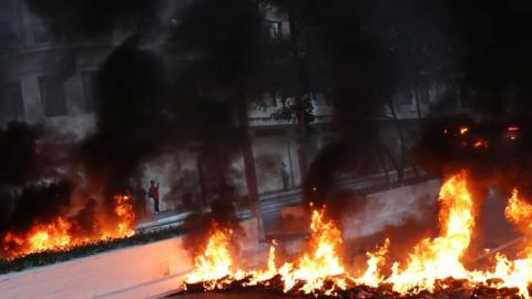 A man stands behind a row of burning tyres blocking the street during a general strike in Sao Paulo