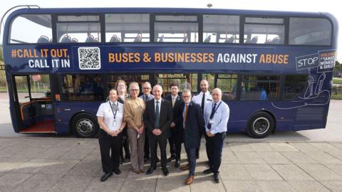 A navy bus with the words "CALL IT OUT" and "BUSES AND BUSINESSES AGAINST ABUSE" on the side