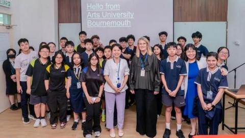 A team photo of Malaysian students with AUB staff in front of a projector with the words 'Hello from Arts University Bournemouth'.