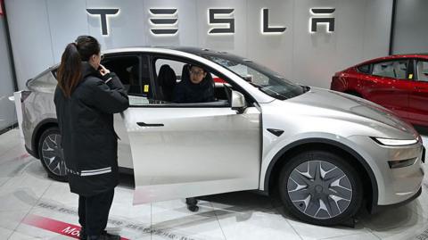 A woman opens the door of a Tesla Model YL electric vehicle as a customer inspects the vehicle