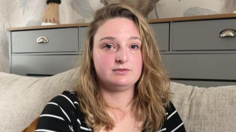 Emily Hotchkiss smiling at the camera. She is sat on a cream sofa.