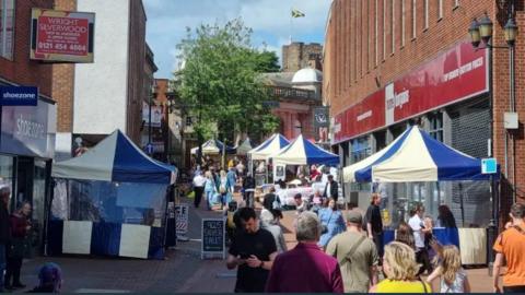 A busy street market with dozens of people looking at stalls