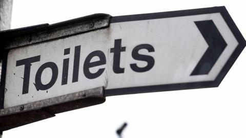 An aged and cracked road sign pointing towards 'Toilets'.