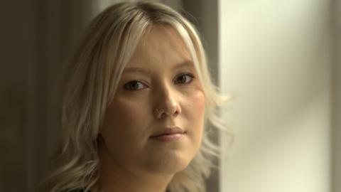 Jessica Matthews looks towards the camera as she stands near a window. She has short blond hair