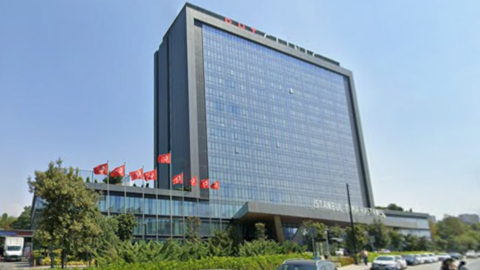 A large, modern, rectangular, grey building with Turkish flags outside