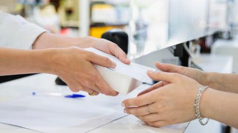 A pharmacist hands a box to a woman in a chemist's shop  