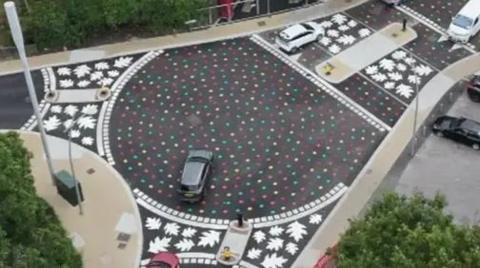 An aerial photo of two roundabouts, with rainbow leaves painted on the tarmac. At each of the the three exists for each roundabout there's a band of white leaves painted across the road.