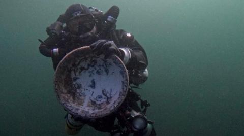 Diver Graeme Bruce in diving gear deep under water holding up a large bowl