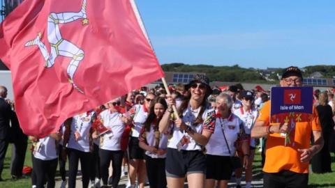 Team Isle of Man headed by Laura Kinley, who is holding the Manx flag smiling.