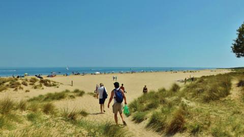 A beach on a sunny day with people walking through the sand dunes