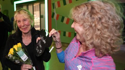 Two women, one holds a bunch of red roses