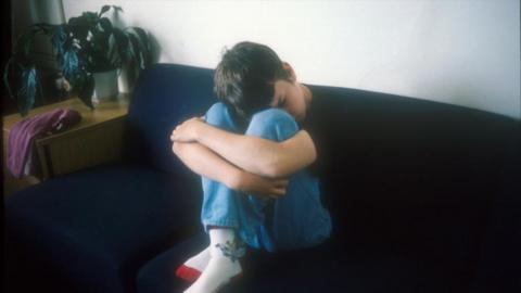 Teenager sitting with head between knees on a sofa