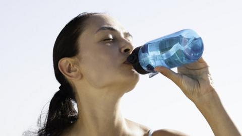 A woman cools off with a drink of water on a hot day