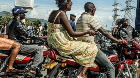 People ride motorbikes behind a truck transporting security forces in Bujumbura on 15 May 2015.