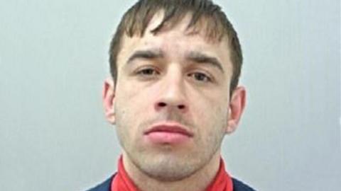 Police custody image of Terrence Kenny with brown hair and eyes wearing a red polo neck top and black jacket.