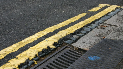 A road with double yellow lines by a grate.