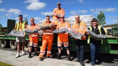 Seven people from East Riding of Yorkshire Council holding bags of compost and wearing hi-vis in front of a trailer