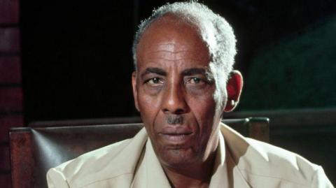 Siad Barre in a safari suit staring at the camera.