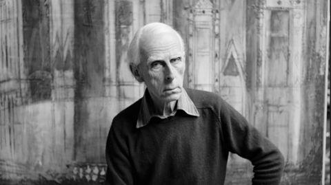 A black and white photo of a man sat in front of a painting