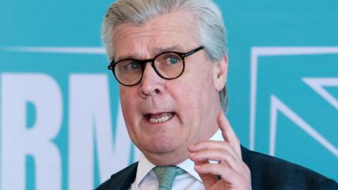 Malcolm Offord, who has grey hair brushed back, in a close-up shot in front of a pale blue background.