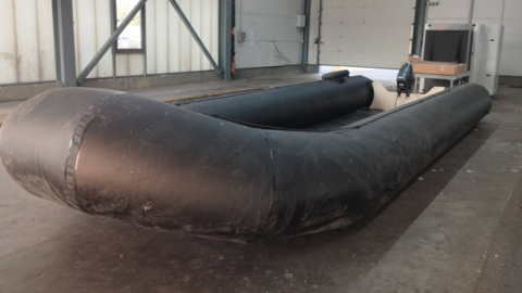 A large, black inflated boat in an empty warehouse. 