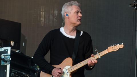 Massive Attack guitarist Angelo Bruschini playing on stage wearing a black jumper and playing a fender telecaster that was auctioned this week