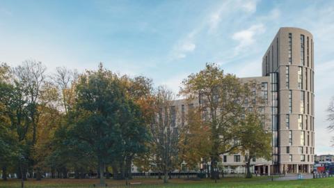 A computer generated image of the new development as seen from Hogland's Park. A tall semi-circular building is on the right of the image, towering above the tree line.