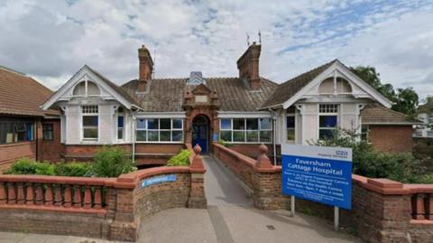 The entrance to Faversham Cottage Hospital. It is a one-storey building with bay windows at each side, and an NHS sign in front.