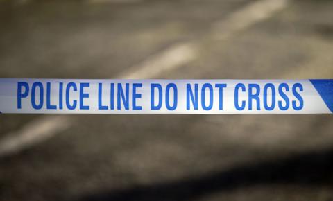 A stock image of police tape against tarmac. It reads "Police line do not cross". 