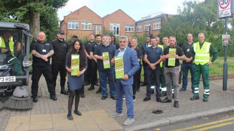 Council leader Muhammed Butt stands with a council team, all holding green anti-fly-tipping posters