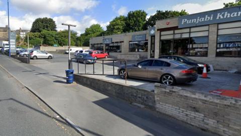 Single-storey hop fronts with large glass windows and a car park in front 