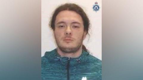 Wiliams, wearing a green and blue hoodie, looks unsmiling in his police mugshot