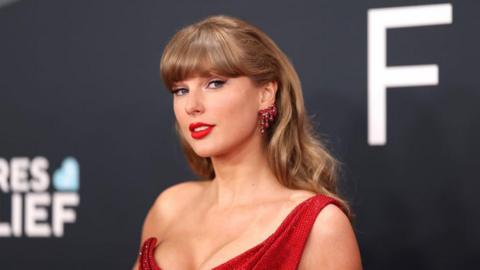 Taylor Swift wears a red dress and looks to the right of the camera