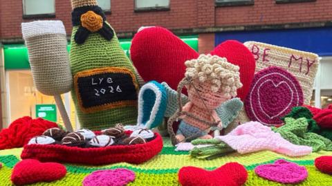 Knitted representations of a Champagne flute, Champagne bottle, box of chocolates, Cupid figure, a heart shape and a Valentines card.