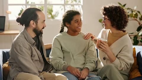 A smiling young adult sits on a sofa in between two parents.