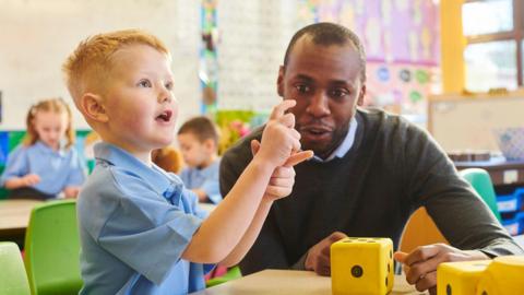 A small boy at school sat next to an adult man in a classroom.