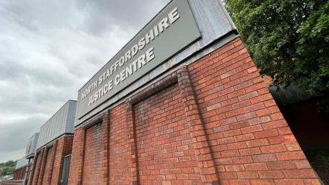 The exterior of North Staffordshire Justice Centre, a red brick building. There is grey signage with white writing that identifies the building.