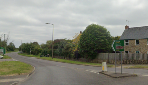 The A619 exit from the De Rodes Arms roundabout in Barlborough, with a cottage with a tree-lined garden and a road sign, to the right.