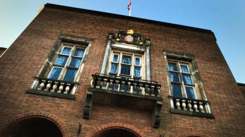 Dudley Council House building with a flag on a pole on the roof. The camera is pointing upwards and three sets of windows are visible.