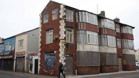 A person walks past boarded up houses in Blackpool town centre on May 3 2024.