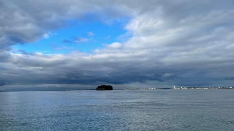 A big blue hole in the cloudy skies above a round fort sat in the middle of the Solent. In the background is Portsmouth with the white Spinnaker Tower in Portsmouth highlighted by sunlight.