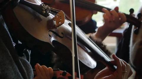 A bow being pulled across the strings of a fiddle.