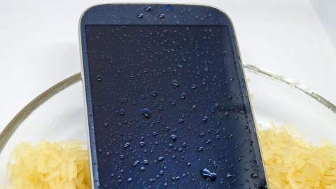 A wet unbranded phone in a bowl of dry rice - stock image