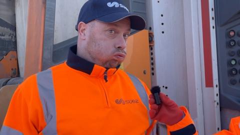 Man in a navy cap and orange hi-vis looking confused
