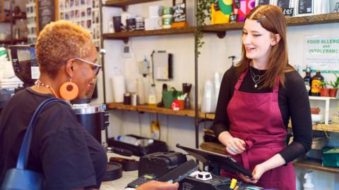 A woman is served by a young woman at the counter of a cafe