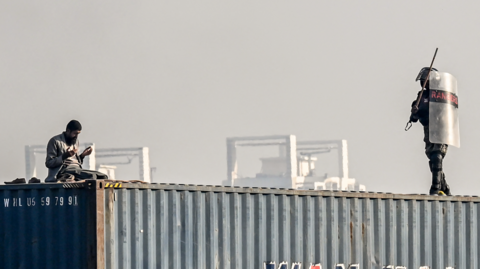 A man is seen praying on top of a shipping container as a paramilitary soldier approaches him during a protest demanding the release of former prime minister Imran Khan, at the Red Zone area in Islamabad on November 26, 2024. 