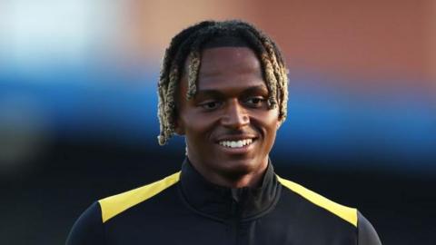 Ethan McLeod in a Wolves black and yellow training top. He has black and blond hair in dreadlocks. He is looking downwards and smiling. 