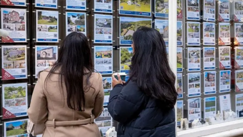 Two women looking at property details in an estate agent's window.