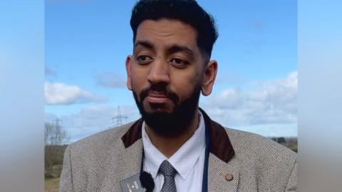 Councillor Armaan Khan stood in front of a green field.