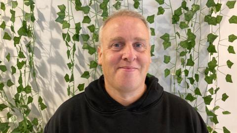 One of the directors of the cafe, Jason Baker, wearing a black hoodie and smiling into the camera.